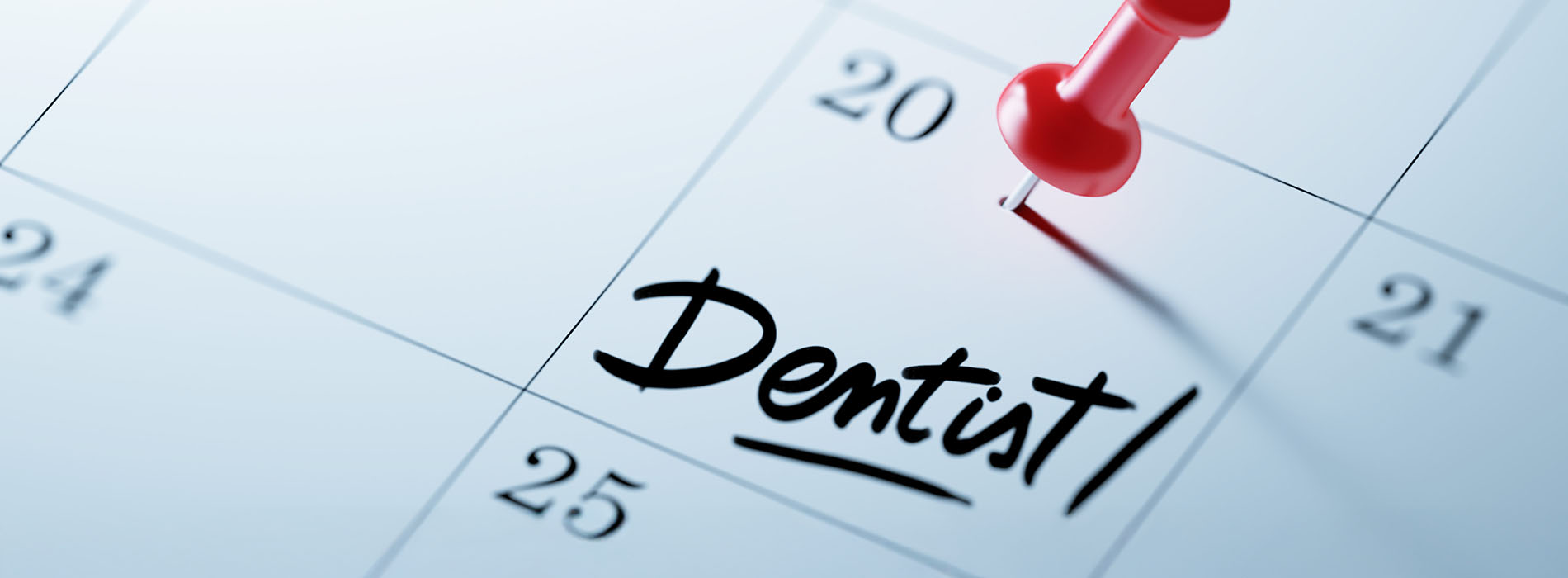 The image shows a calendar with the word  dentist  written on it, placed next to a red push pin on a light blue background.