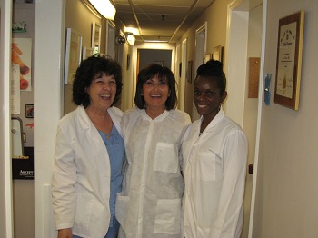 Three individuals posing together, likely in a professional setting, with two women wearing white lab coats and one woman in casual attire.