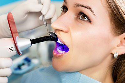 A woman undergoing dental treatment with a device that appears to be a dental implant tool inserted into her mouth.