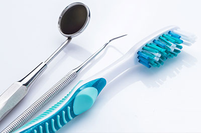 An assortment of dental tools including a toothbrush with blue bristles, a dental mirror, and a pair of tweezers displayed on a white background.