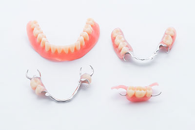 The image shows a set of dentures with visible teeth, displayed on a white surface against a light grey background.