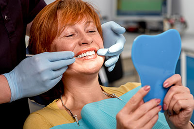 A woman in a dental chair receiving a teeth cleaning, with a dental hygienist applying toothpaste and a blue dental impression material.