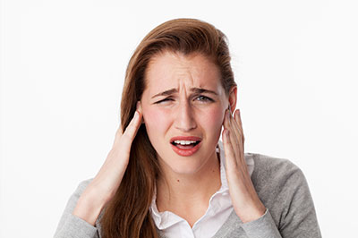 The image shows a woman with her hand on her head, looking concerned, against a plain background.