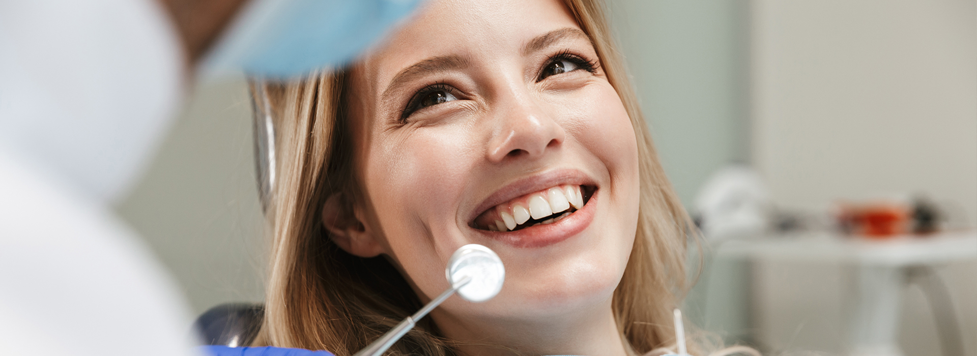 Woman smiling at camera while seated in dental chair during dental exam.