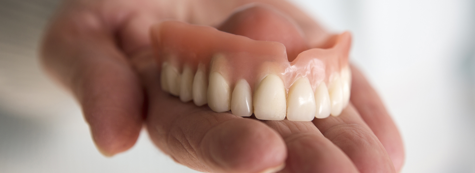 Dentures being held by a person s hand against a blurred background.