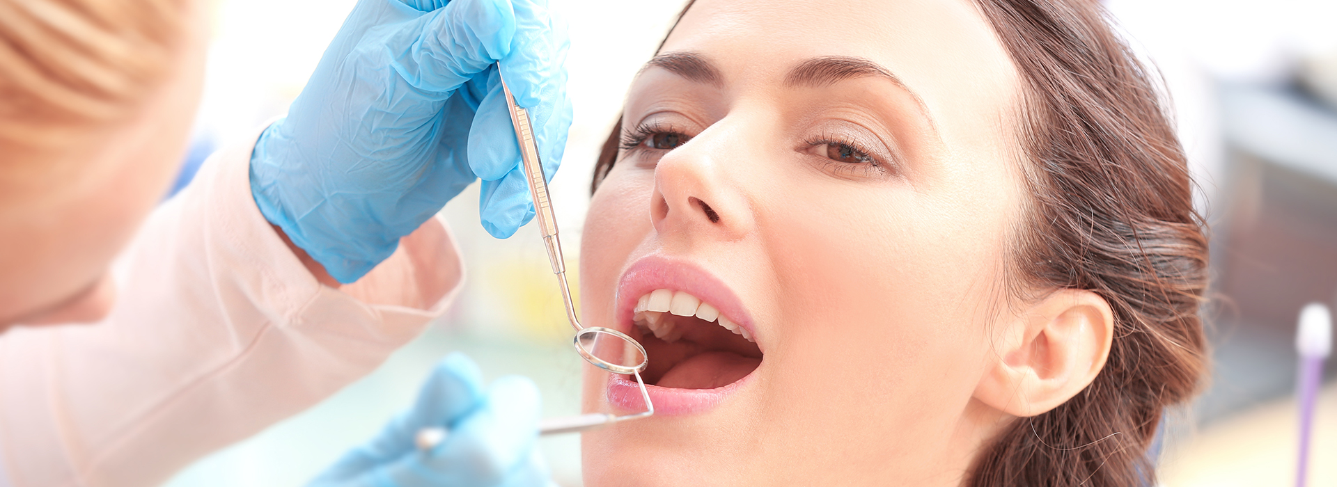 A woman receiving dental care from a dentist, with her mouth open wide, and a close-up view of the dental instruments being used.