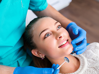 An image of a dental professional performing a procedure on a patient s teeth while she smiles.