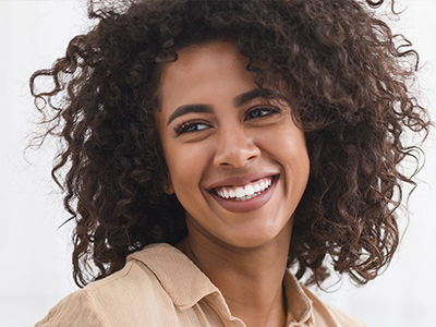 The image shows a woman with curly hair smiling at the camera. She has a radiant smile and appears to be happy.